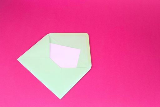 A closeup shot of a white envelop with a pink note on a pink background