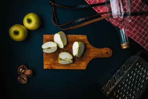 A top view of cut apples on a wooden board on the table with utensils on