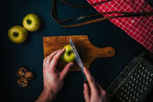 A top view of a hand cutting an apple on a wooden bord