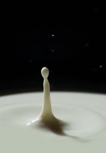 A vertical shot of a drop of milk falling on a black background