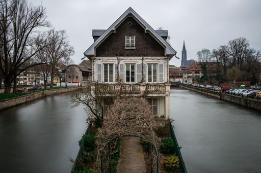 An old building surrounded by water and greenery under a cloudy sky in Strasbourg in France