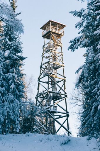 A vertical shot of a wooden watchtower among the snow covered trees