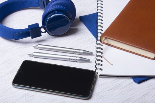 A top view of  a cell phone with headphones, notebooks, and pens on a surface