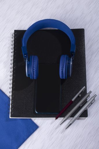 A top view of  a cell phone with headphones, notebooks, and pens on a surface