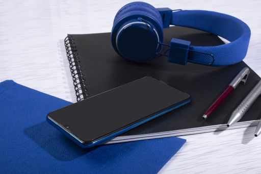 A top view of  a cell phone with headphones, notebooks, and pens on a surface