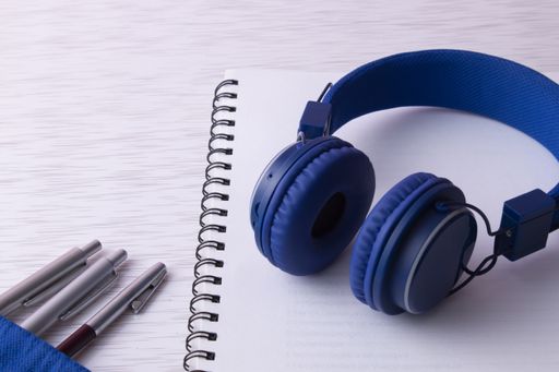 A shot of a notebook with pens  and blue headphones