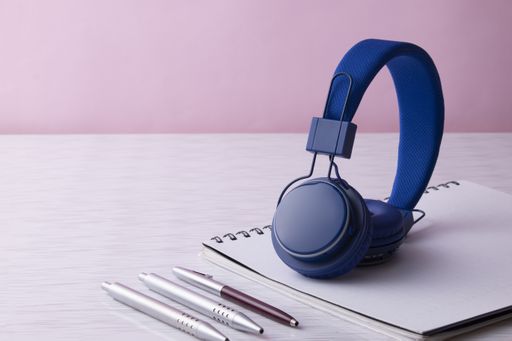 A shot of a notebook with pens  and blue headphones