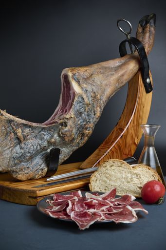 A vertical shot of Spanish Jamon with bread, cherry tomato, and oil on a gray backgr