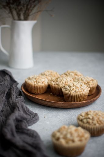 A vertical shot of muffins on a wooden plate on the table decorated with flowers in a vase