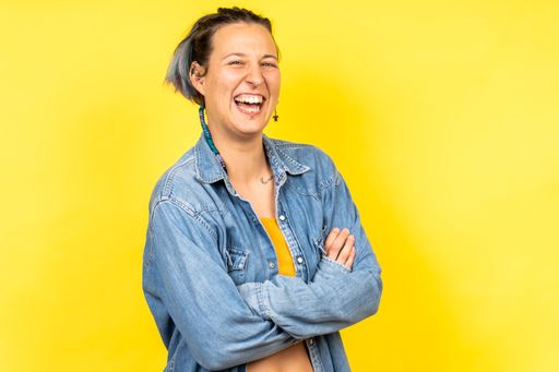 A pretty Caucasian woman posing with crossed hands and laughing on a yellow background