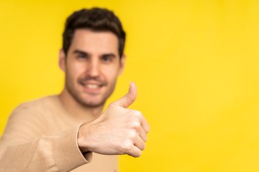 A handsome Caucasian man showing a thumbs up and posing on a yellow background