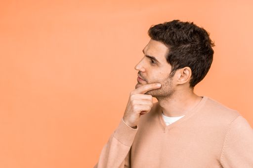 A handsome Caucasian man looking thoughtfully at the left side of the photo on an orange background