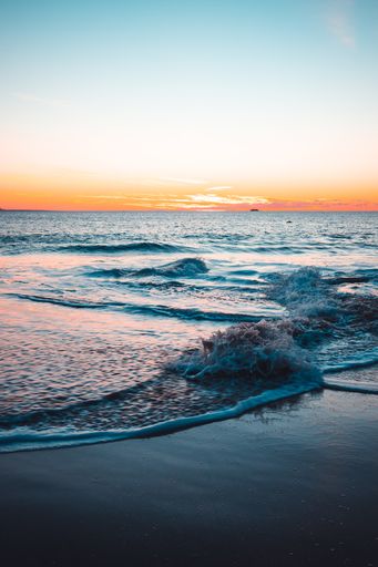 A vertical shot of an ocean and the seashore under a sunset sky