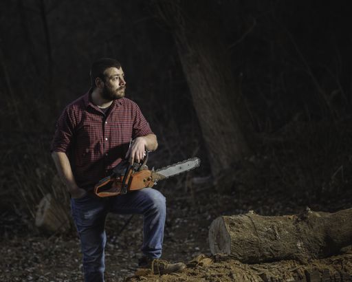 A shallow focus of a Caucasian lumberjack holding a chain saw beside a fallen tree in the woods