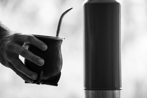 A grayscale selective focus shot of a hand holding a  calabash mate cup with straw - yerba mate tea infusion