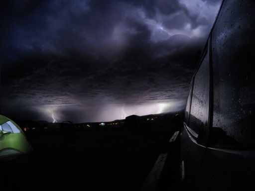 A black car on the road under the storm clouds during the lightning at night time
