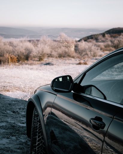 A vertical shot of a black modern car parked in the wilderness
