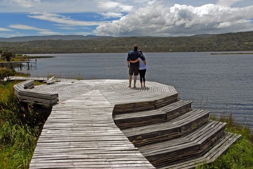 A couple standing on a wooden pathway and looking at the sea while hugging each other