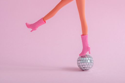 Plastic doll feet on a small disco ball on a pink background