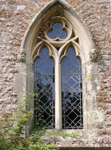 Exterior of rural English church window, in stone, with interesting carved heads supporting the base of the arch, located in England, United Kingdom.