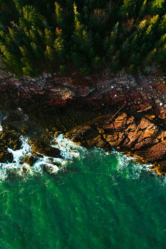 An aerial view of the rugged coastline of New Brunswick, Canada, featuring vibrant teal waves crashing onto the shore