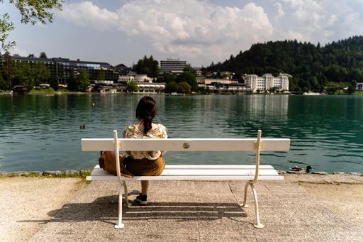A female sitting on a white bench near Lake Bled in the background of buildings and trees in Slovenia