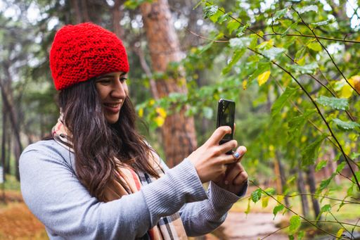 A young caucasian female taking a photo while walking in a park in autumn