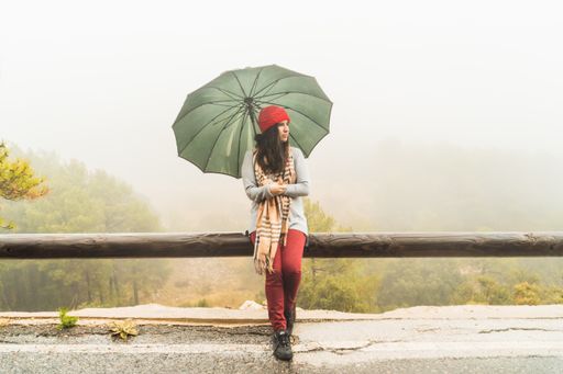 A young caucasian female posing in a park with an umbrella on a rainy day