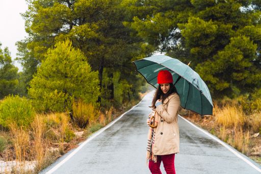 A young caucasian female walking in a park with an umbrella on a rainy day