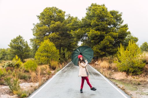 A young caucasian female walking in a park with an umbrella on a rainy day