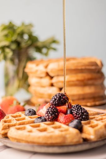 A vertical shot of honey pouring on waffles with berries