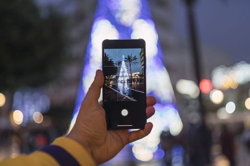 A man's hand holding smartphone and taking a photo of the Christmas tree