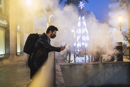 A shallow focus shot of a young European male in a black mask using his smartphone
