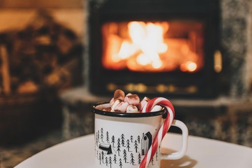 A mug of cocoa or hot chocolate with powdered marshmallows and candy cane by the fireplace