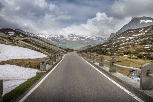 A straigh paved road going through beautiful nature scenes under a rainy cloudscape