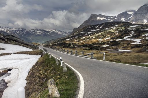 A curvy paved road going through beautiful nature scenes under a rainy cloudscape