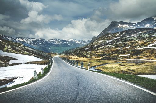 A curvy paved road going through beautiful snow-cavered nature scenes under a rainy cloudscape