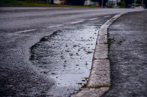 A selective focus shot of raindrops falling into a puddle by the sidewalk