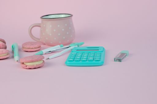 A shot of a mug with macaroons and calculator on a pink background