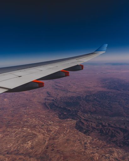 A vertical shot of an airplane wing with the landscape in the background