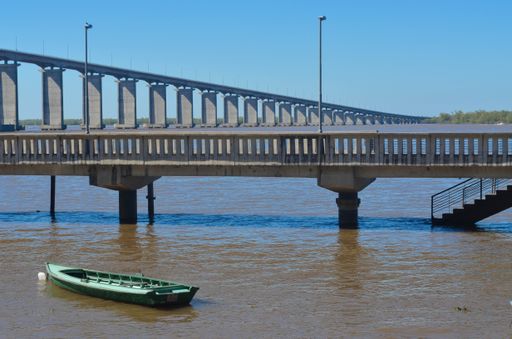 A shot of a green boat in the water under the stone bridge