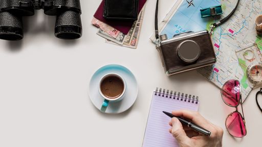 A male hand holding a pen and writing in notebook [inscription] on the table with traveling objects