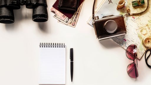 A top view of a pen and a notebook on the table with other traveling items
