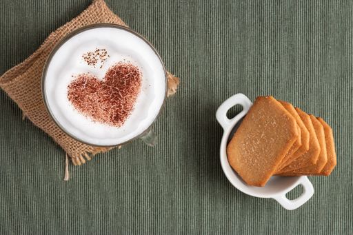 A closeup shot of a table surface with a heart shaped latte and biscuits