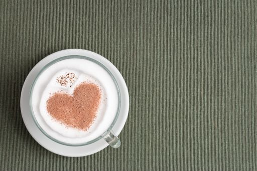 A cappuccino cup with a heart shape on the surface on the gray background with copy space from the right side - the St. Valentine's day concept