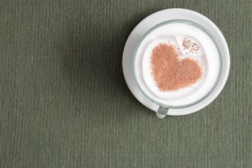 A cappuccino cup with a heart shape on the surface on the gray background with copy space from the left side - the St. Valentine's day concept