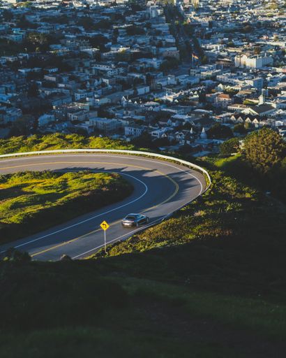 A vertical shot of a curvy road down the hill with buildings in the distance