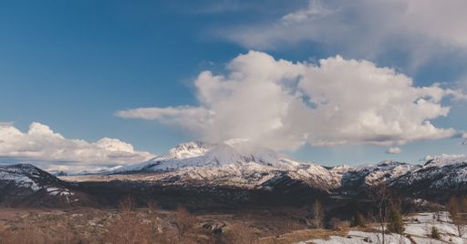 A wide shot of snowy mountains in the distance under a blue cloudy  sky