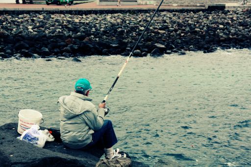 A senior male sitting on a pier and fishing in Spain