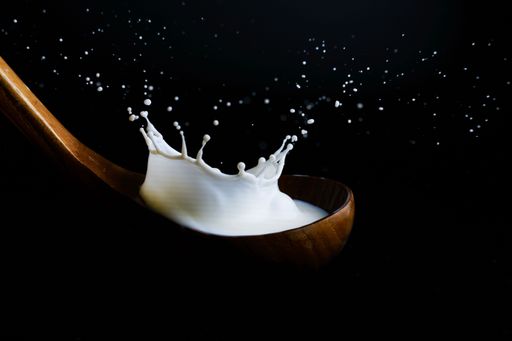 milk splashing on a wooden ladle, with splash effect and black background